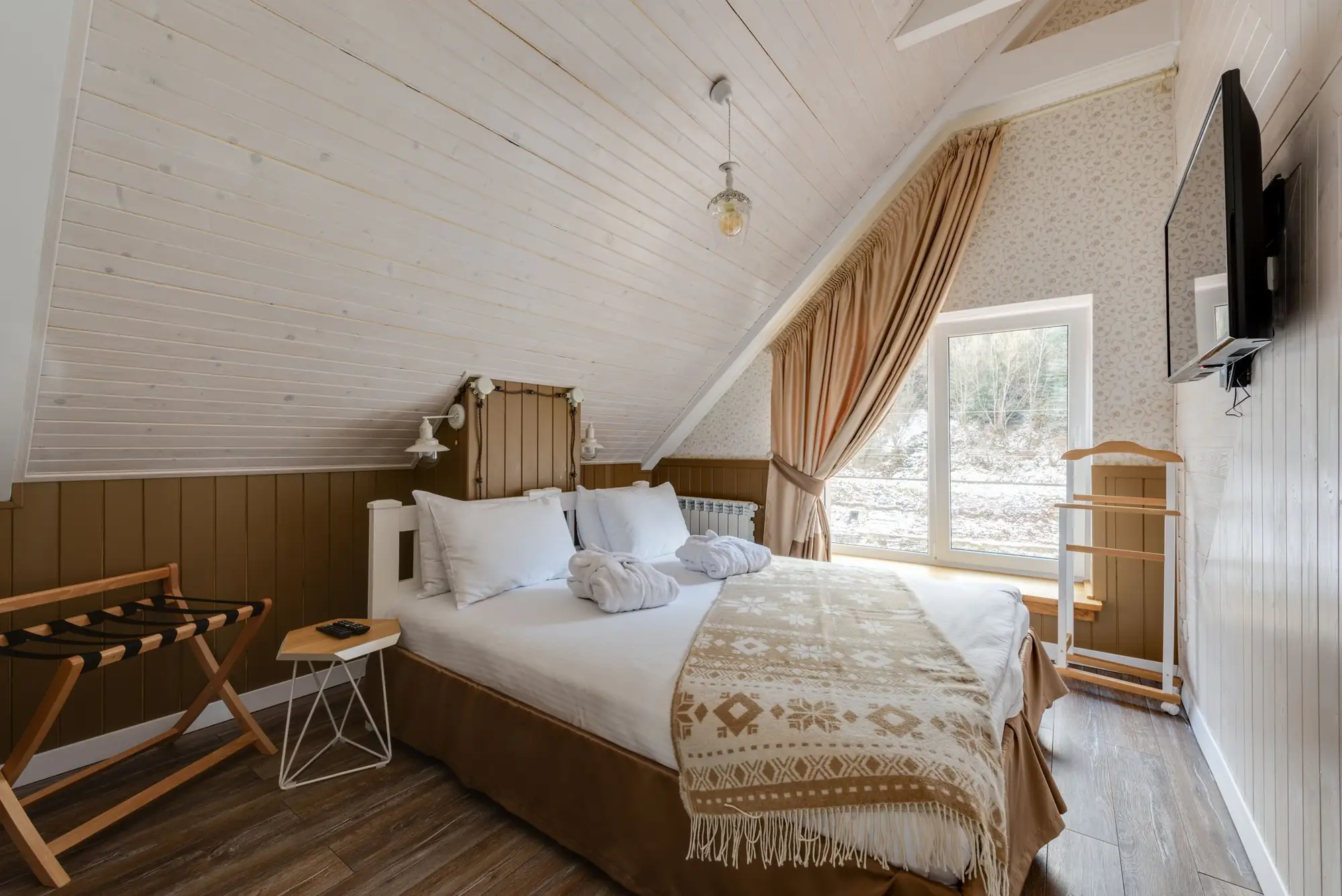 A calm cottage bedroom under a sloping ceiling, with linen bedding and a wool throw